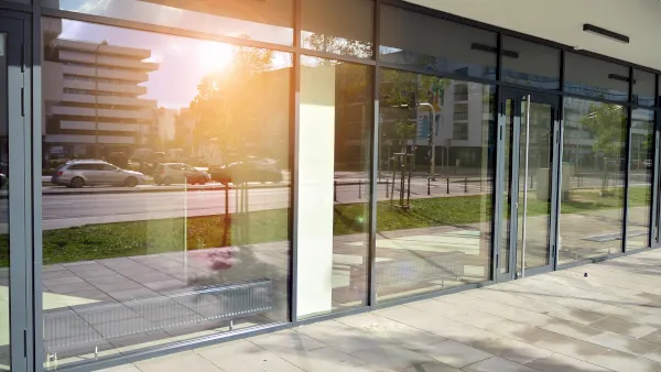 Eine Reihe großer Glasfensterscheiben spiegelt an einem sonnigen Tag in Düsseldorf die Straße, die Autos und die Bäume im Freien. Der Bürgersteig und eine leere Gewerbefläche sind durch das Glas sichtbar.