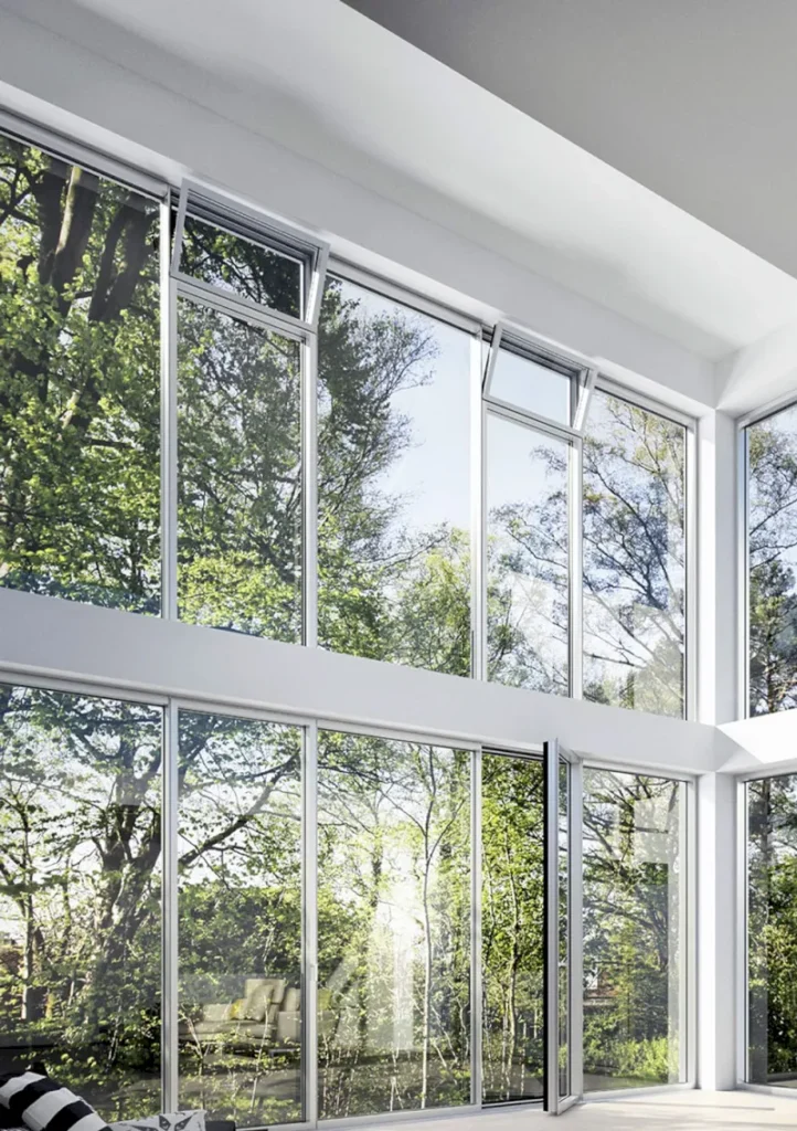 Hohe, raumhohe Glasfensterscheiben in einem modernen Raum in Erkrath geben den Blick auf grüne Bäume und das Sonnenlicht frei und schaffen eine helle und luftige Atmosphäre mit Spiegelungen auf dem Glas.