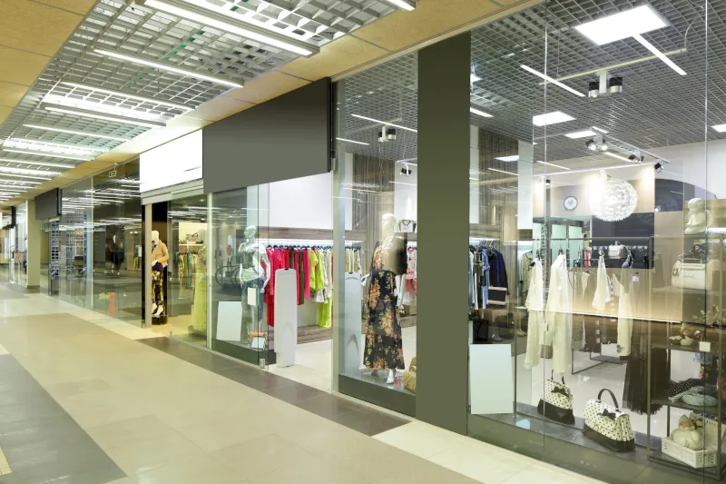 Ein modernes Bekleidungsgeschäft mit Schaufensteranlagen und Glaswänden in Velbert-Neviges, in dem Schaufensterpuppen in verschiedenen Outfits und Regale mit farbenfroher Kleidung ausgestellt sind. Helle Beleuchtung und geflieste Böden vervollständigen das stilvolle Erscheinungsbild.