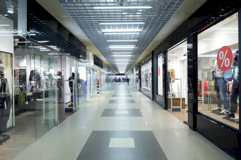 Ein moderner, überdachter Gang eines Einkaufszentrums in Velbert-Neviges mit Schaufensteranlagen auf beiden Seiten, Kleiderauslagen und Verkaufsschildern. Der hell erleuchtete Gang ist menschenleer.